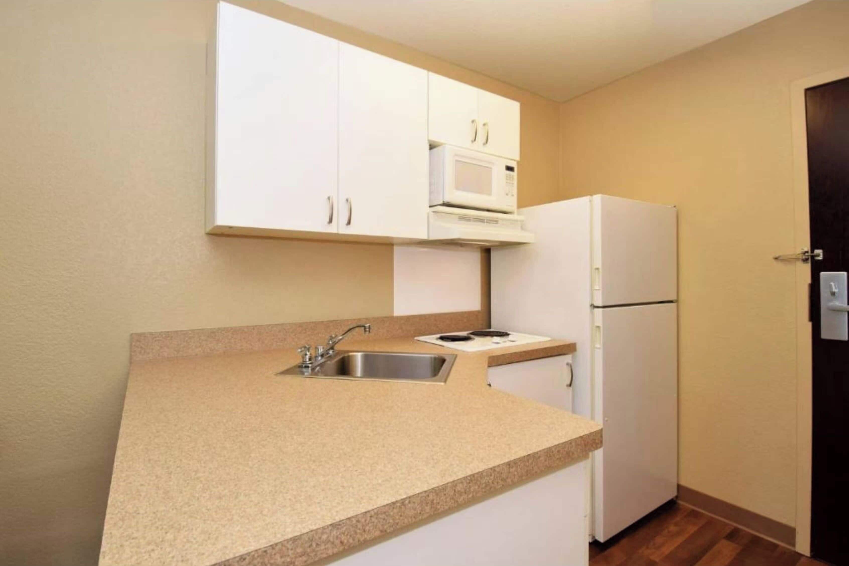 A compact kitchen with white cabinets, a microwave, a refrigerator, and a granite countertop.