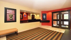 A hotel lobby with a reception desk, a bench, and a striped carpet. - Studio 6 Corporate Extended Stay Washington, D.C. Germantown MD (Germantown)