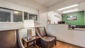 Un espace d’accueil comprenant un comptoir de réception, deux fauteuils en cuir, une lampe et un panneau mural indiquant « HomeTownne Studios ».