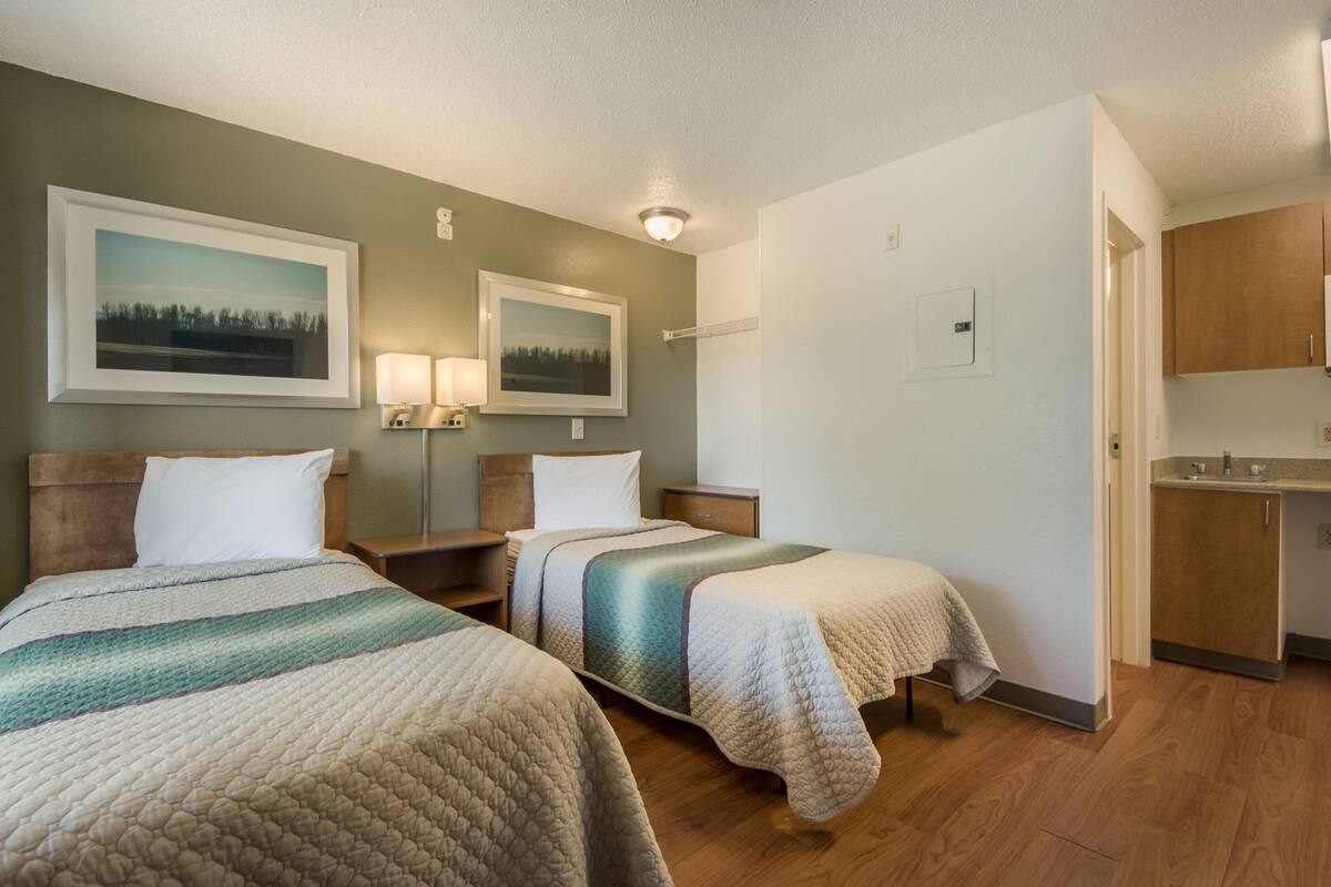 A hotel room with two beds, a small kitchenette, and a bathroom.