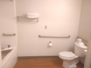 A small, single-occupancy bathroom with a toilet, a handrail, a towel rack, and a roll of toilet paper.