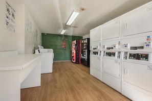 A laundry facility with multiple washing machines and dryers, a green wall, and a wooden floor. - HomeTowne Studios by Red Roof Dallas - Mesquite (Mesquite)
