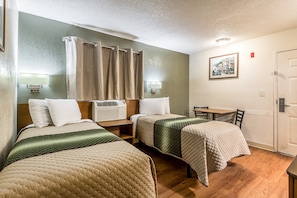 A hotel room with two beds, a desk, a chair, a table, a shower curtain, a wall-mounted air conditioner, a wall-mounted lamp, and a framed picture on the wall.
