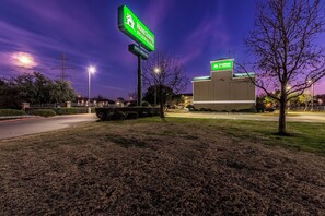 A building with a green sign indicating 'Home Town Studios' with a parking lot in front. - HomeTowne Studios by Red Roof Dallas - Mesquite (Mesquite)