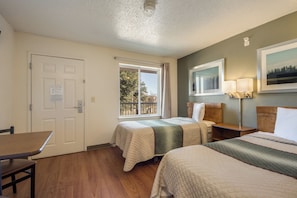 Une chambre d’hôtel avec deux lits, un bureau, une fenêtre donnant sur des arbres et un tableau accroché au mur.