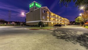 A multi-story hotel with a prominent sign, a parking lot, and a street view at night.