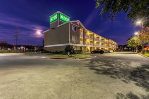 Un hotel de varios pisos con un letrero llamativo, un estacionamiento y vista a la calle de noche.