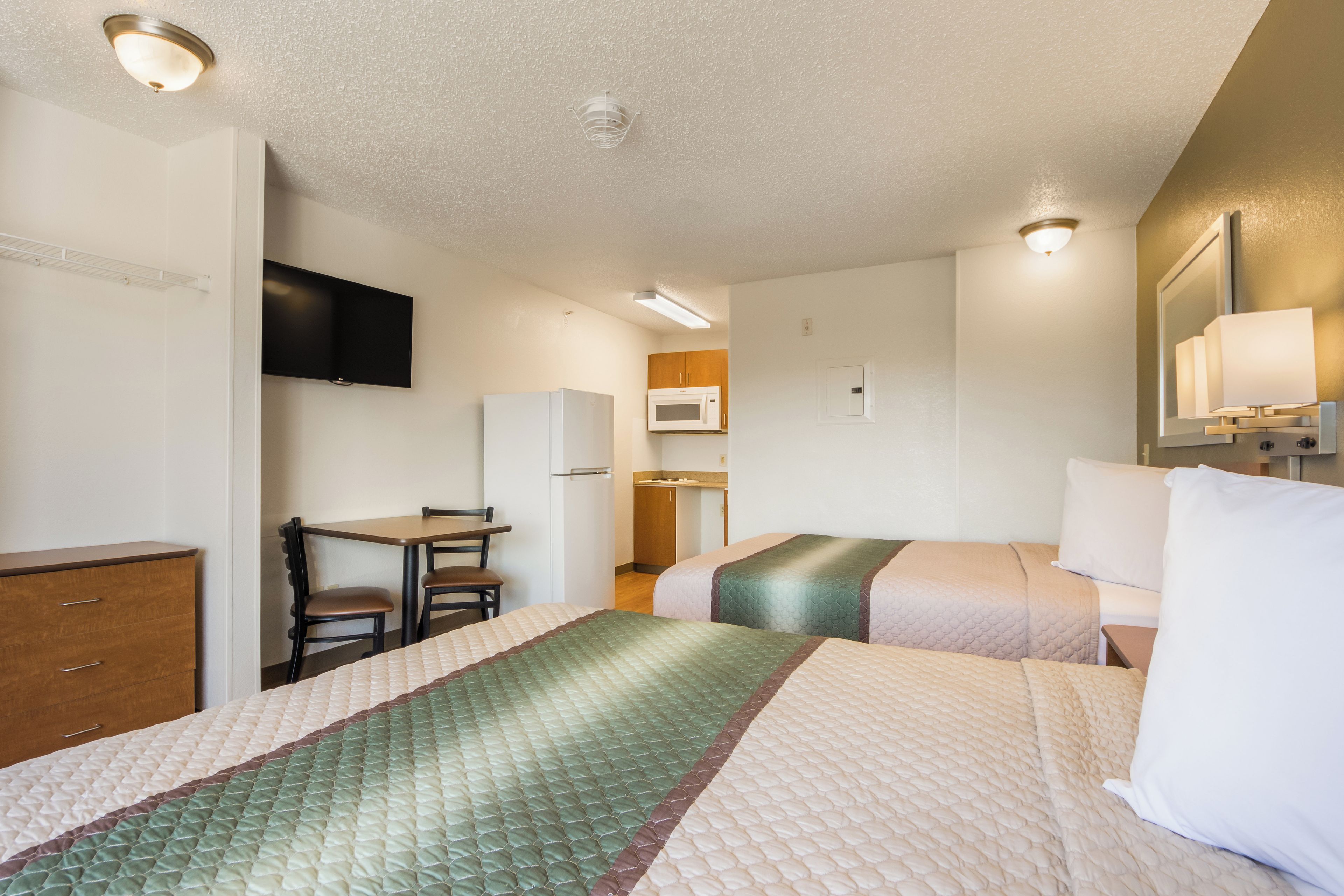 Una habitación de hotel con cama, escritorio, silla, televisor, microondas y armario.