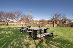 Un espacio al aire libre con césped, mesas de picnic y seto.
