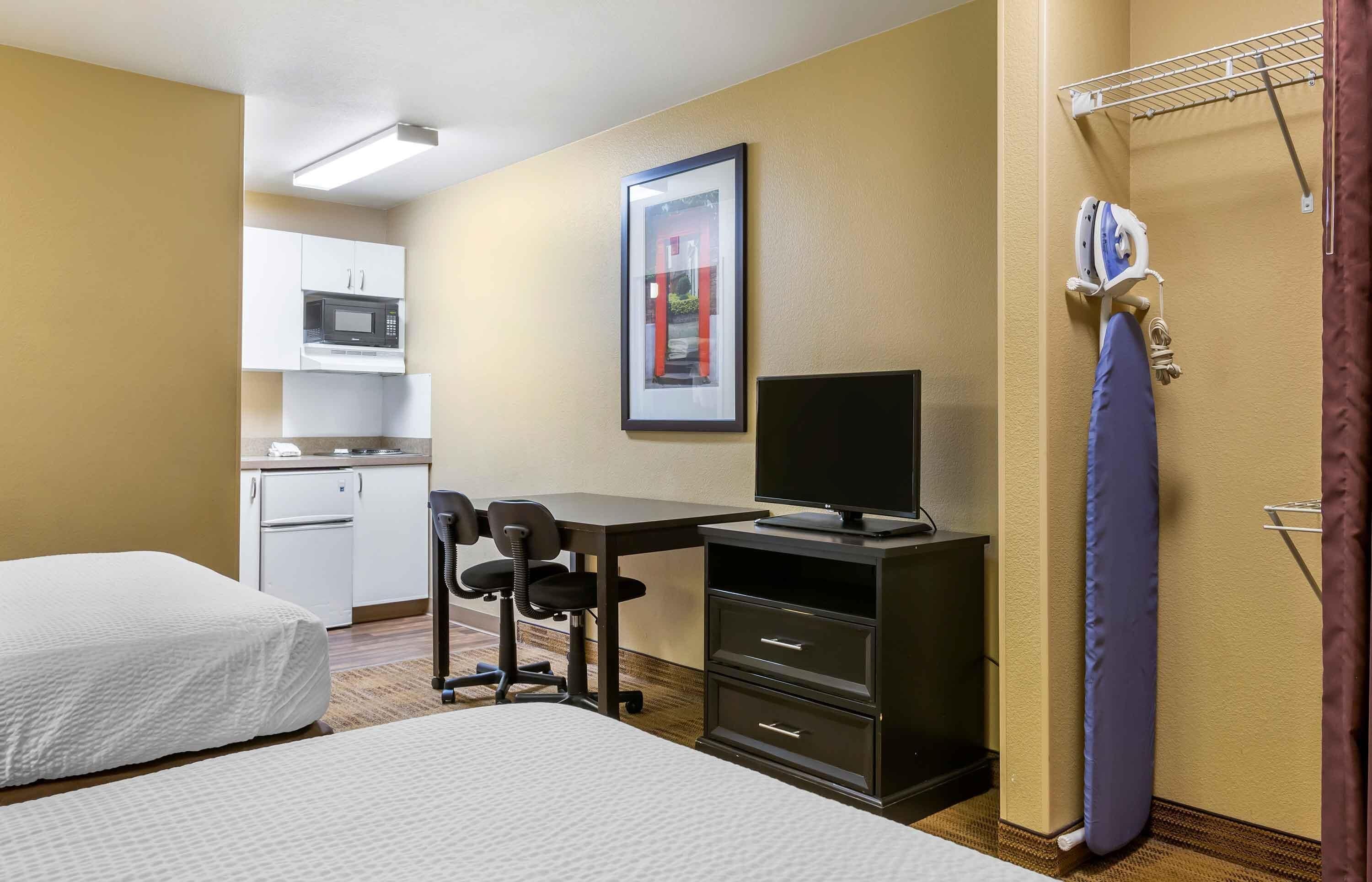 A hotel room with two beds, a desk with a computer, a microwave, and a small kitchenette.