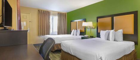 A hotel room with two beds, a desk, a television, and a window with curtains.