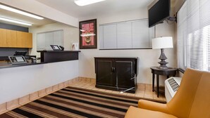 A modern hotel room with a reception desk, a flat-screen TV, a cabinet, a lamp, and a striped rug.