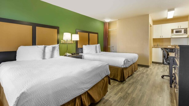 A hotel room with two beds, a desk, a microwave, and a shower.