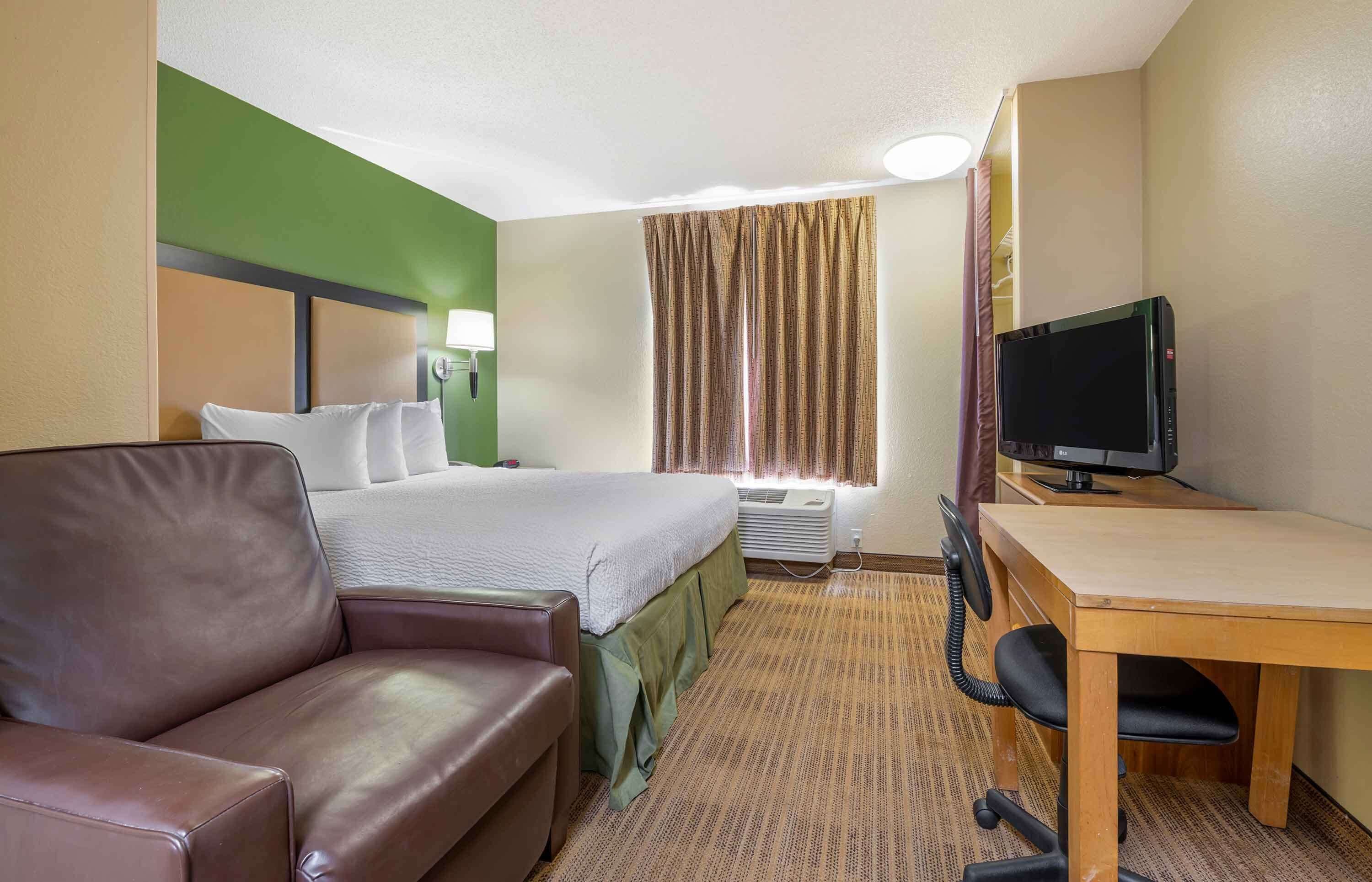 A hotel room with a bed, a desk with a computer, a leather sofa, and a window with curtains.