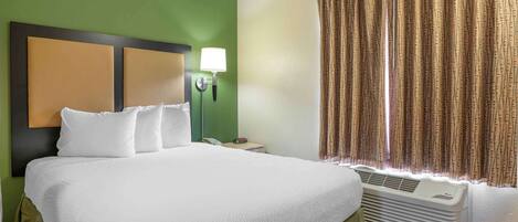 A hotel room with a large bed, a bedside lamp, a heater, and a window with curtains.