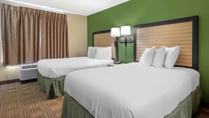 A hotel room with two beds, a green wall, and a window with curtains.