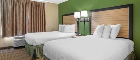 A hotel room with two beds, a green wall, and a window with curtains.