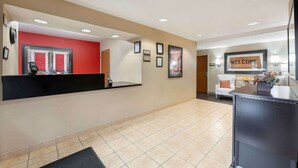 A hotel reception area with a red wall, a 'WELCOME' sign, framed certificates, and a reception desk.