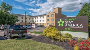 A sign for Extended Stay America suites with a parking lot and a building in the background.