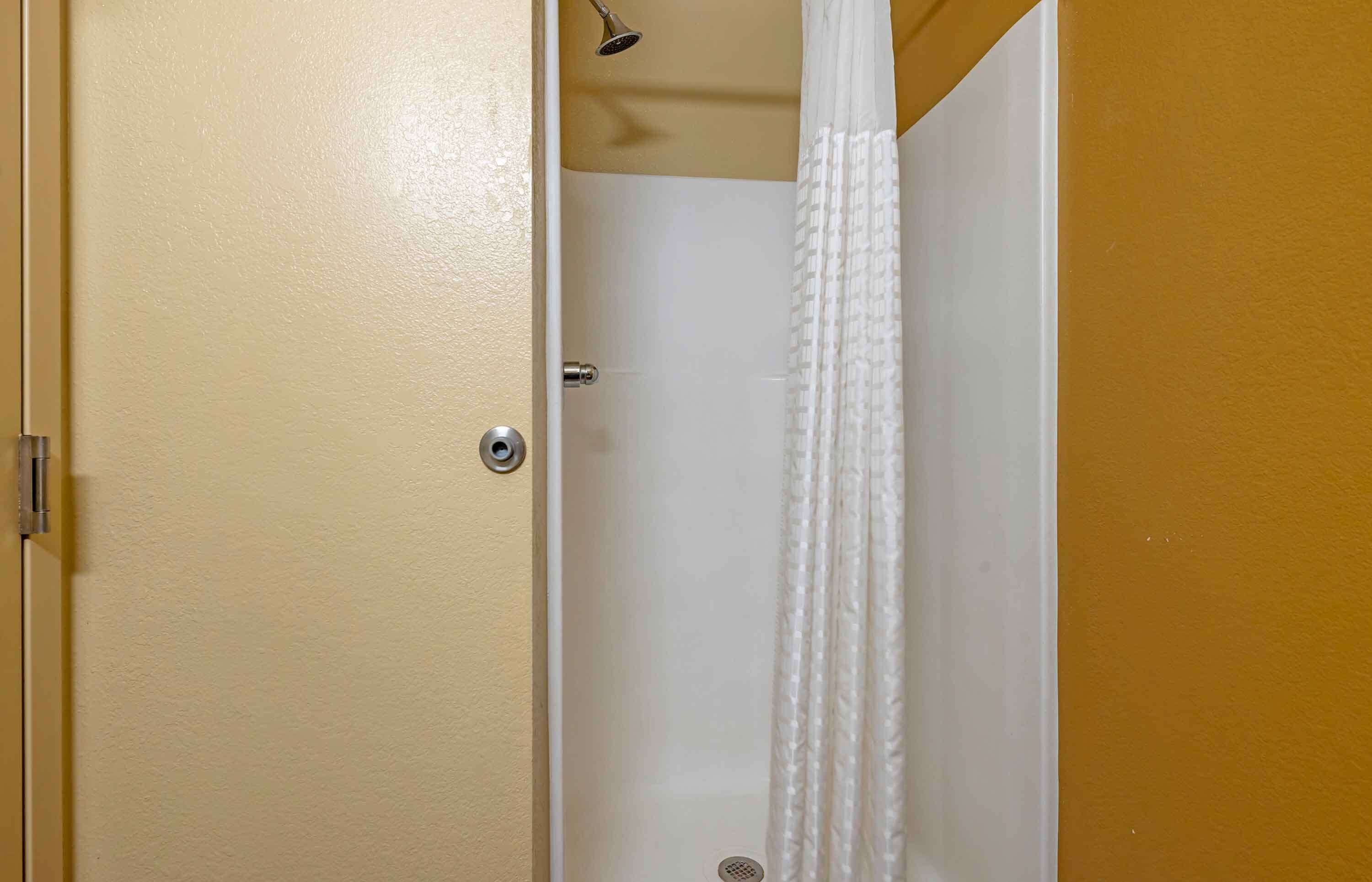 A bathroom with a white shower curtain, a visible showerhead, and a door with a silver handle.