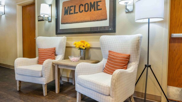 A reception area with two upholstered chairs, a small table with a vase of flowers, a welcome sign, and a floor lamp.