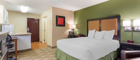 A hotel room with a bed, desk, chair, and a small kitchenette.