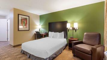 Una habitación de hotel con cama, escritorio, silla y mesita de noche.