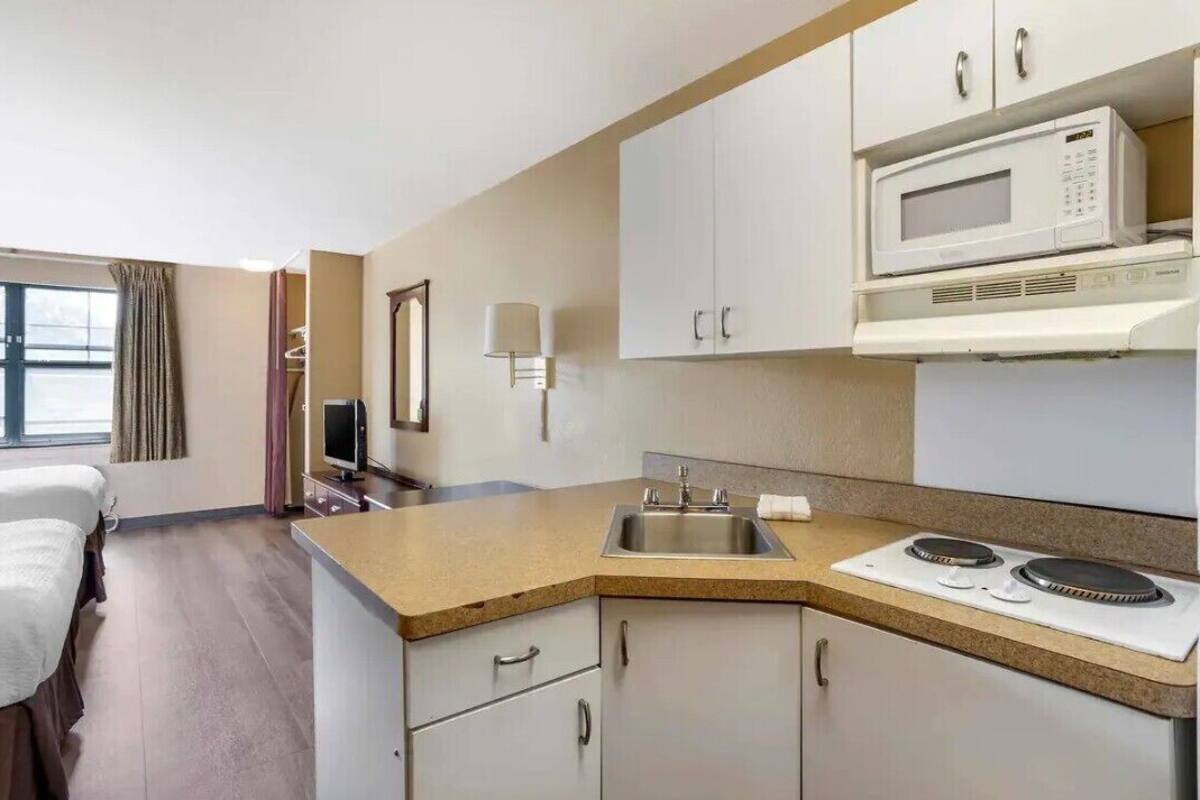 Habitación de hotel con kitchenette, una cama, televisor y ventana con cortinas.