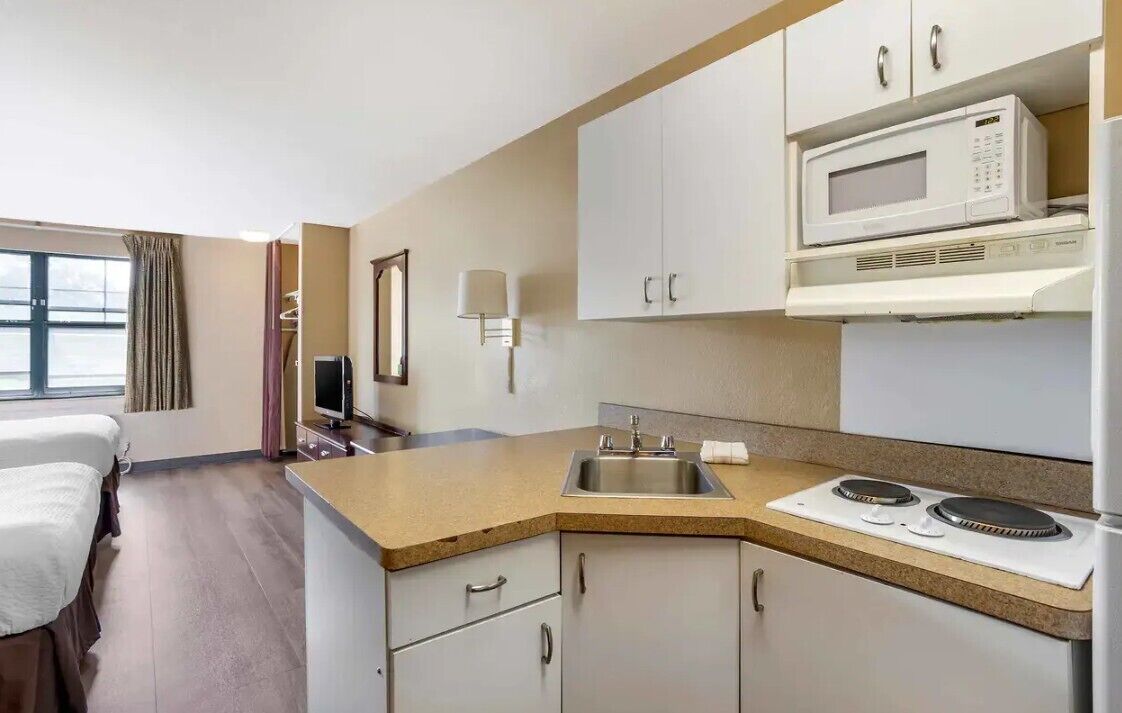 A hotel room with a kitchenette, a bed, a TV, and a window with curtains.