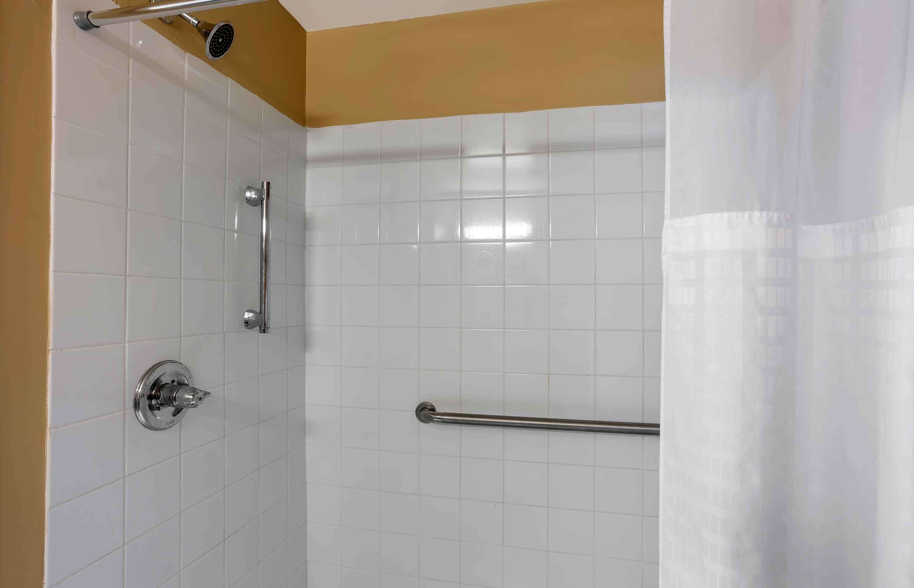 A shower area with white tiled walls, a glass door, and a metal grab bar.