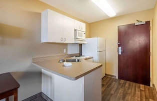 Una cocina pequeña con armarios blancos, microondas, refrigerador y piso de madera.