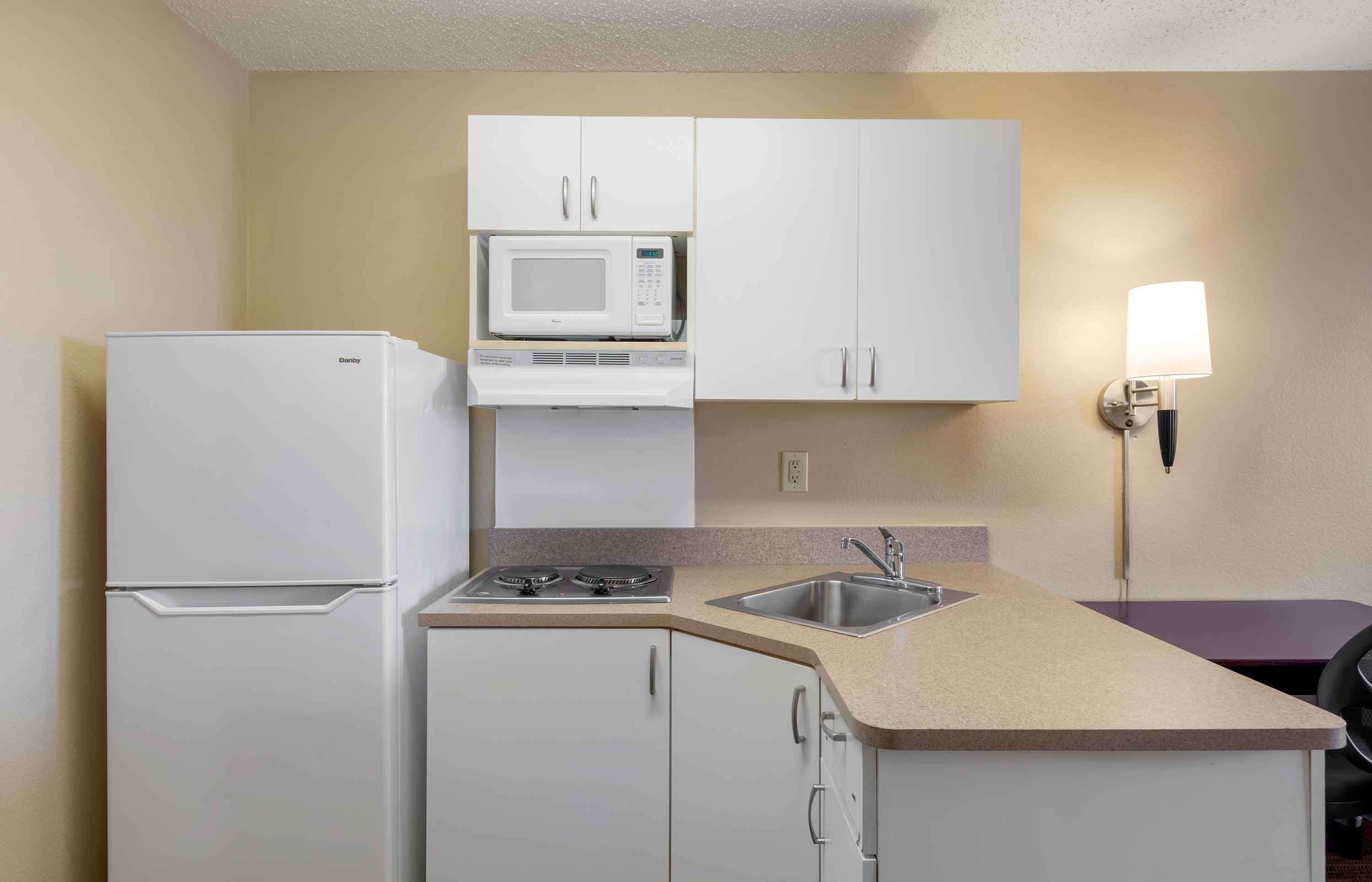 A compact kitchen with white cabinets, a microwave, a stove, and a sink.