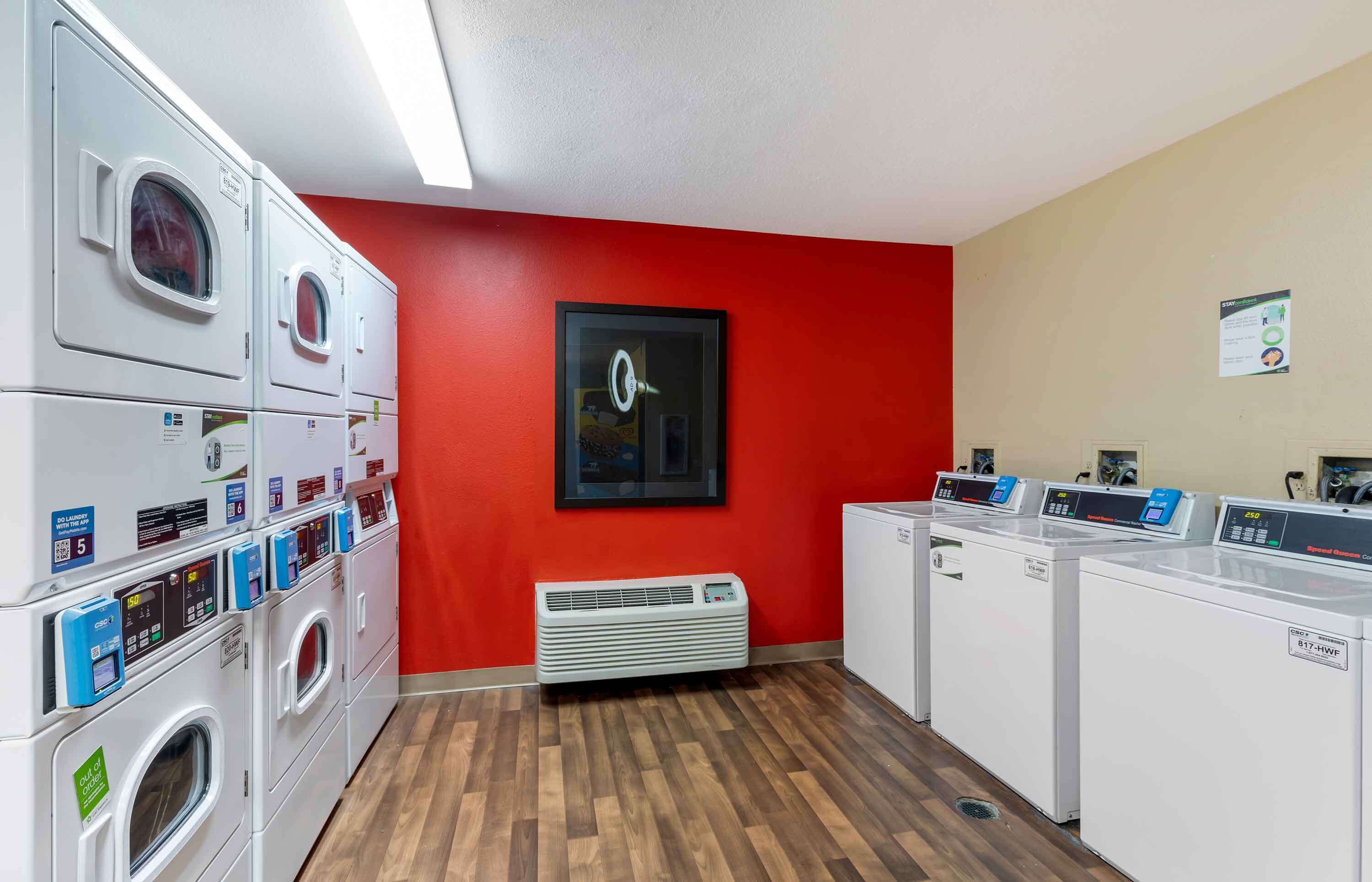 A laundry room with multiple washing machines and dryers, a red wall, and a framed picture.