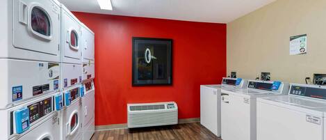 A laundry room with multiple washing machines and dryers, a red wall, and a framed picture.