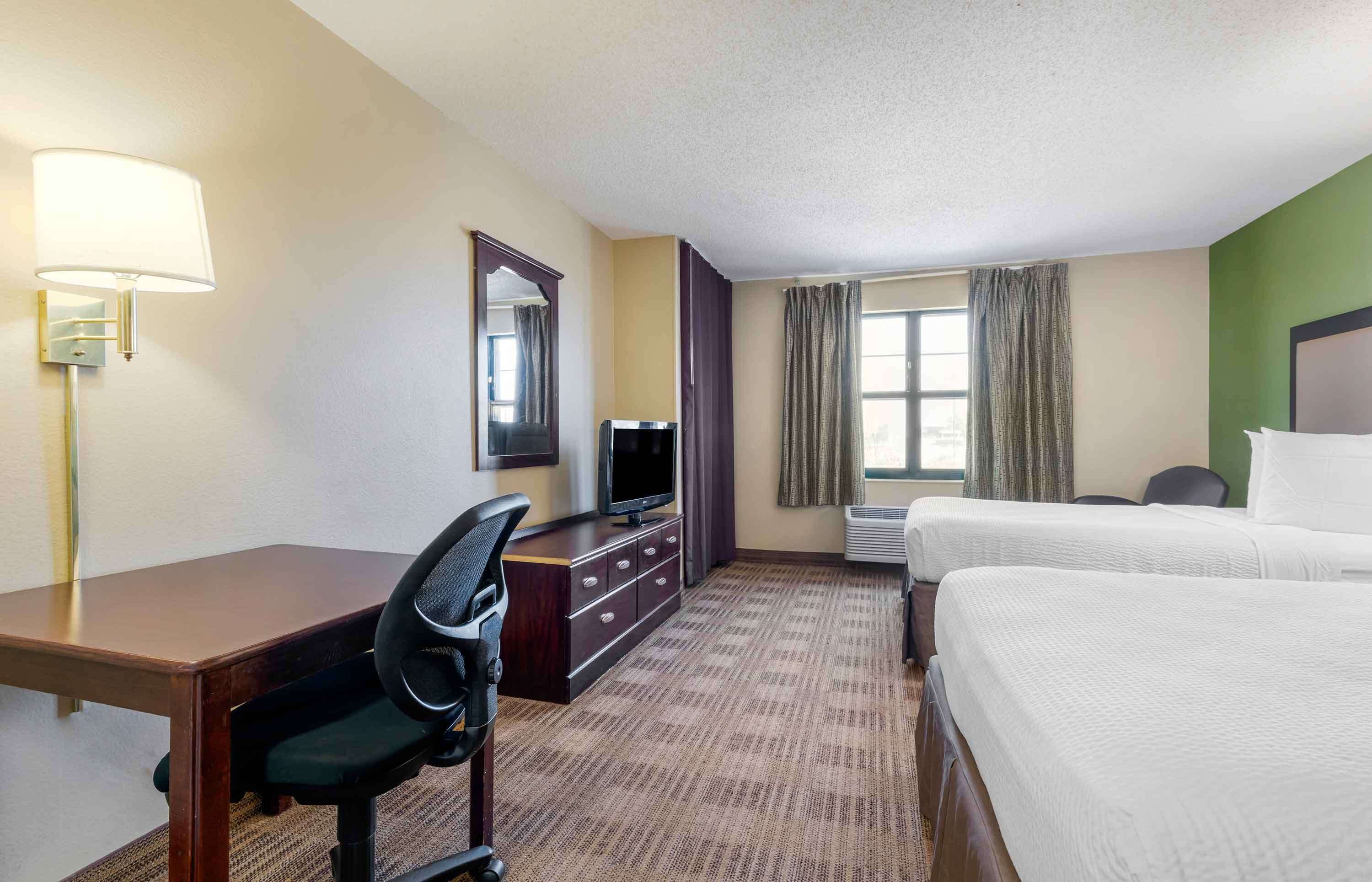A hotel room with a desk, chair, television, two beds, and a window with curtains.