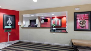A reception area with a red wall, a reception desk, a bench, and a framed artwork on the wall.