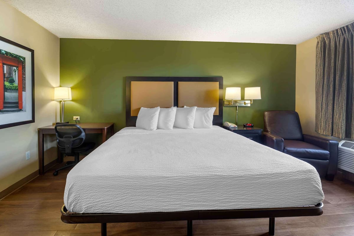 Habitación de hotel con una cama grande, un escritorio, dos sillas, una lámpara de escritorio y un aire acondicionado de pared.