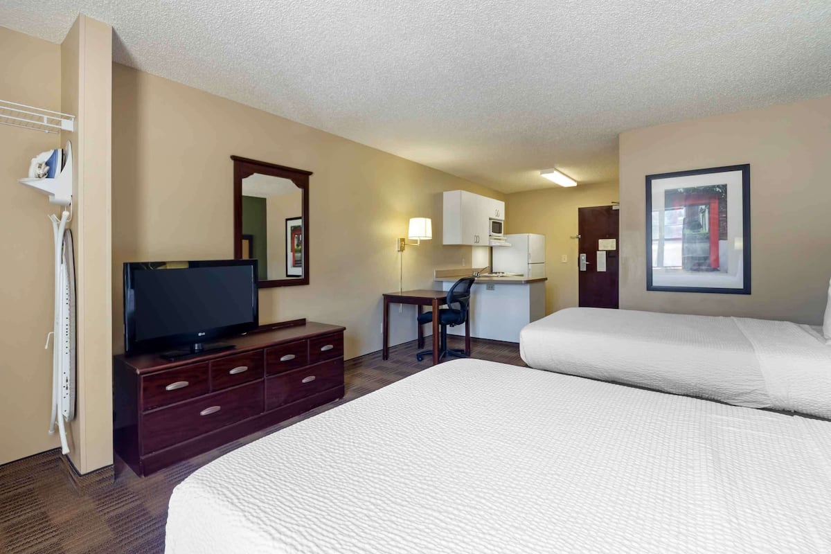 Habitación de hotel con dos camas, televisión, escritorio, microondas y refrigerador.