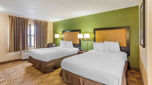 A hotel room with two beds, a large window with curtains, a wall-mounted air conditioner, and a framed picture on the wall. - Extended Stay America Select Philadelphia Malvern Great Vall (Malvern)