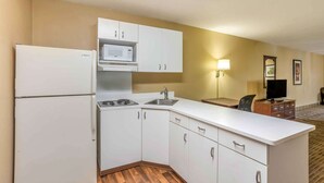 A compact kitchen with white cabinets, a microwave, a sink, and a stove. There is a small seating area with a chair and a TV. - Extended Stay America Select Philadelphia Malvern Great Vall (Malvern)