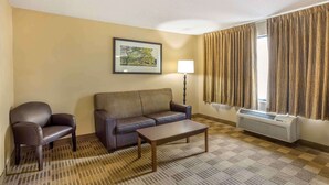 A hotel room with a sofa, armchair, and a table. There is a lamp, a window with curtains, and a picture on the wall. - Extended Stay America Select Philadelphia Malvern Great Vall (Malvern)