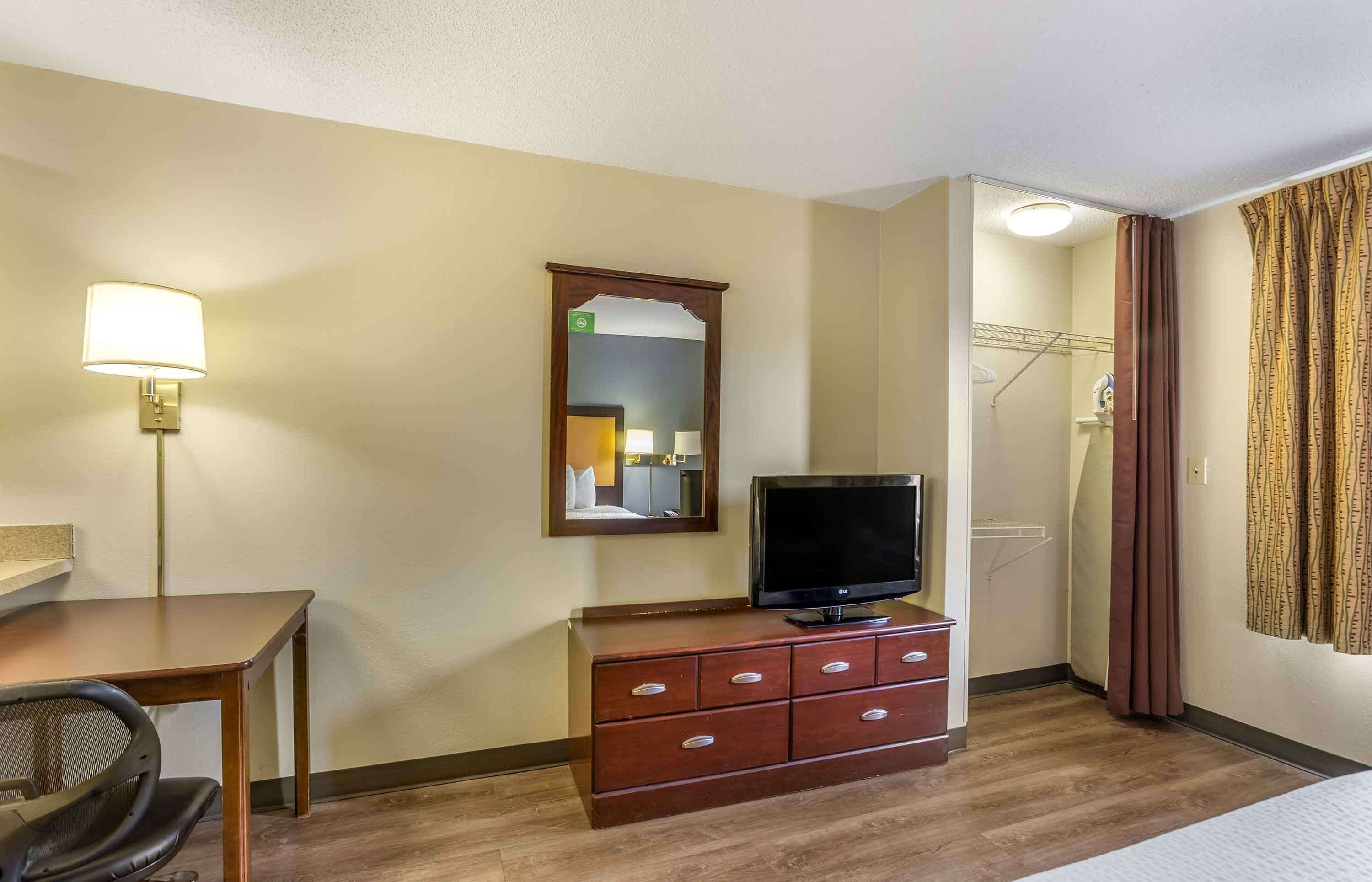 A hotel room with a wooden desk, a television on a dresser, a mirror, and a shower area.