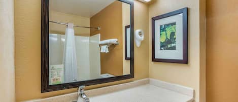 Un baño con un espejo grande, un lavamanos, un perchero para toallas y un cuadro en la pared.