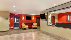 A hotel reception area with a red wall, a reception desk, a flat-screen TV, and two leather chairs. - Extended Stay America Select Philadelphia Malvern Great Vall (Malvern)