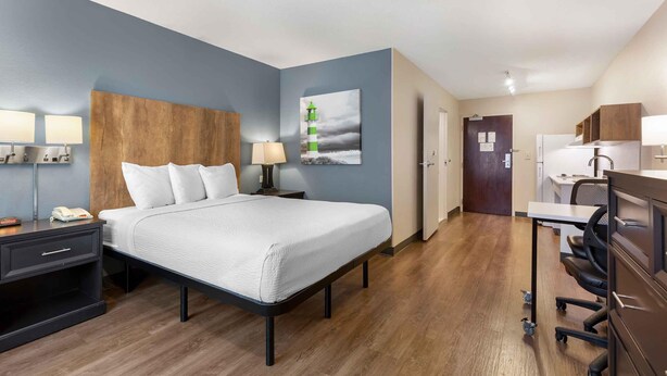 Habitación de hotel con cama, mesitas de noche, escritorio, silla, refrigerador y puerta.