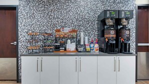 Una estación de autoservicio para bebidas con varias opciones de café, variedad de aperitivos y una pared decorativa con textura.