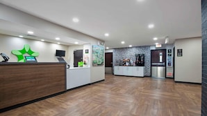 Zona de recepción de hotel con un mostrador de madera, un quiosco digital, un gran logotipo verde, un mapa y una máquina de café.