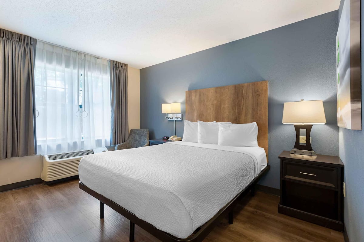 Een hotelkamer met een groot bed, twee bedlampen, een stoel, een bureau en een raam met gordijnen.