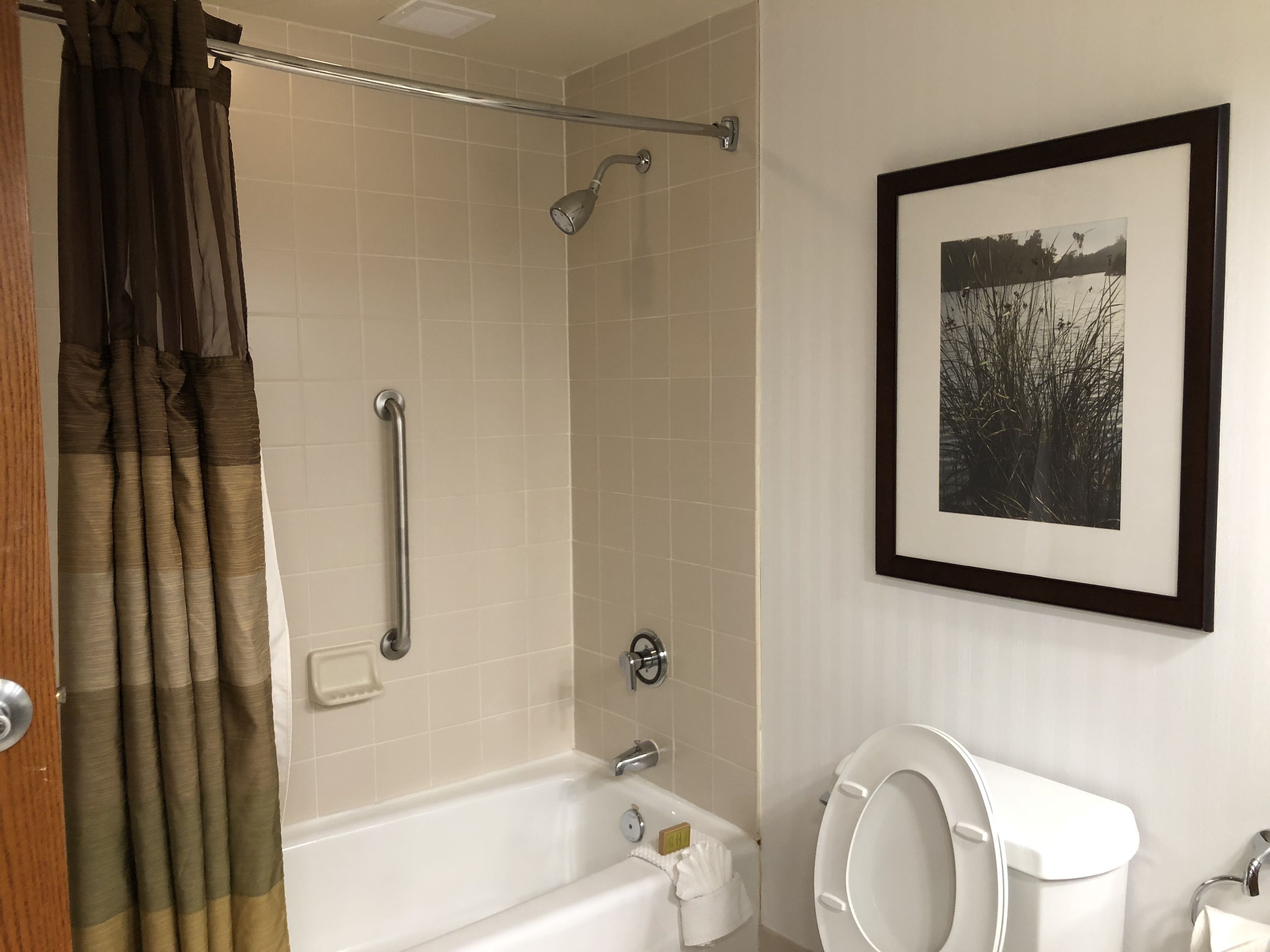 Ein Badezimmer mit Badewanne, Toilette und Dusche inklusive Haltegriff.