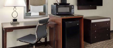 Habitación de hotel con escritorio, silla, microondas, refrigerador, televisor y espejo.